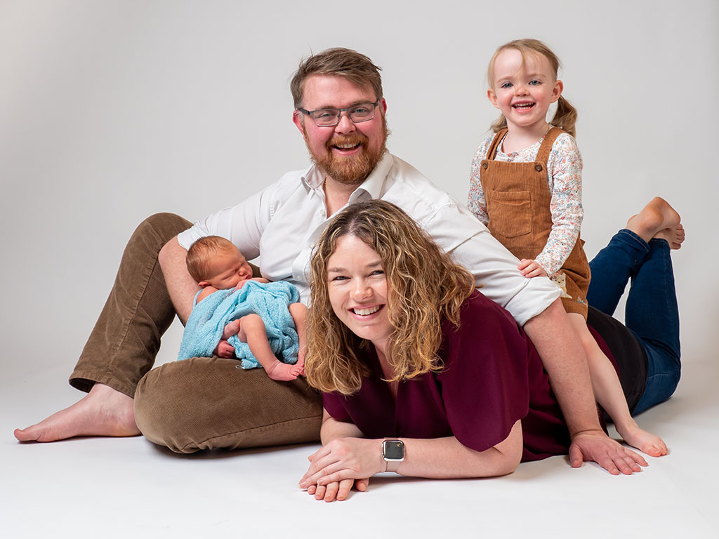 dad sitting on floor with mum daughter and newborn baby taken by family newborn photographer in Braintree